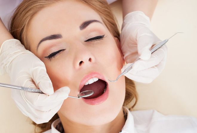 dentist with white gloves on holding dentistry forceps near patient's mouth.