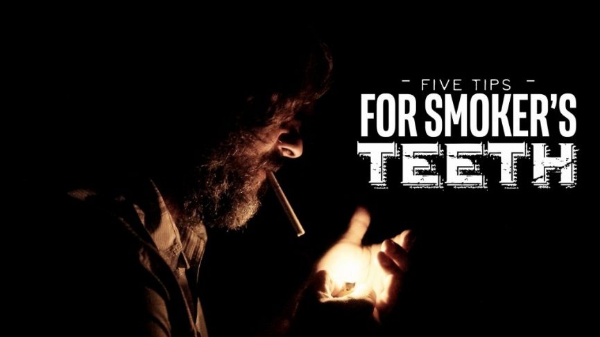 a man with a beard, lighting a cigarette. The scene is dark, with the only light source being the flame from a lighter, illuminating the man's face and hand. The background is entirely black, creating a stark contrast. The text overlay reads, "Five Tips for Smoker's Teeth," emphasizing dental care advice specifically for smokers.